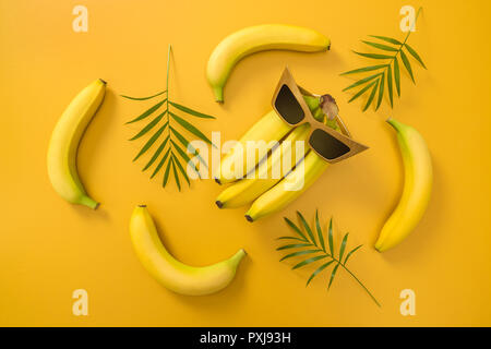 Bananas, sunglasses and palm leaves on vibrant yellow background. Tropical summer theme. Stock Photo