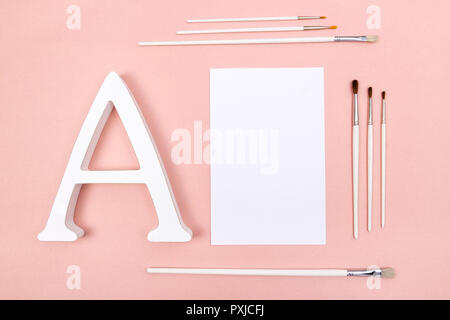 Blank sheet of paper, letter A and white paintbrushes, on pastel pink background. Stock Photo