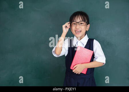 Asian Chinese little Girl in uniform standing against green blackboard in classroom Stock Photo