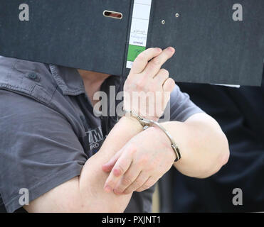 Gera, Germany. 23rd Oct, 2018. The defendant sits in handcuffs in the jury courtroom of the regional court and hides his face behind a file. The 66-year-old is accused of murdering a ten-year-old girl from Weimar in August 1991. Only after 27 years the crime could be solved. Credit: Bodo Schackow/dpa-Zentralbild/dpa/Alamy Live News Stock Photo