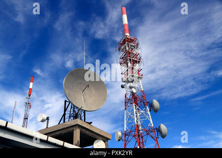 Wide view of several kind of communication antennas and a red and white tower against beautiful deep blue sky with some white clouds Stock Photo
