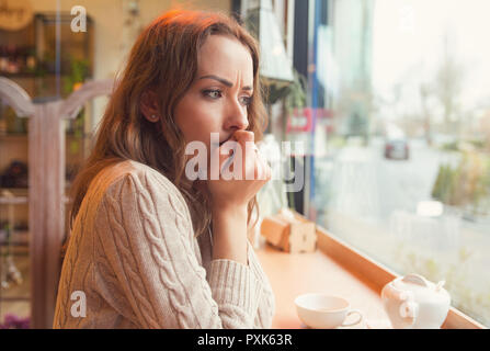 Nervous worried young woman biting nails and looking away sitting alone in a coffee shop Stock Photo