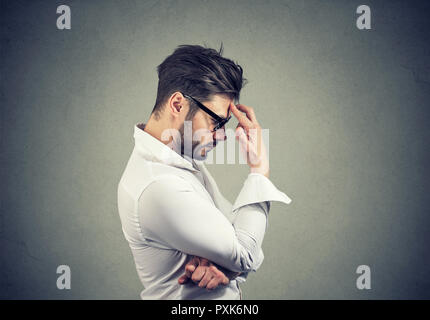 Side view of bearded man in glasses and white shirt touching forehead being in depression and full of thoughts Stock Photo