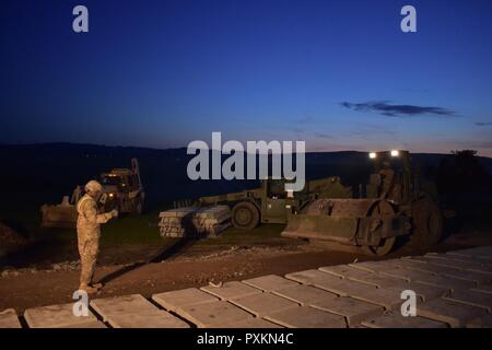 Soldiers from the 465th Company, 926th Engineer Battalion, 926th Engineer Brigade, United States Army Reserves, compact the base layer for the approach lane to an ammunition-loading dock at the Joint National Training Center, Cincu, Romania, as part of their nighttime operation for Resolute Castle 2017. Resolute Castle is an exercise strengthening the NATO alliance and enhancing its capacity for joint training and response to threats within the region. Stock Photo