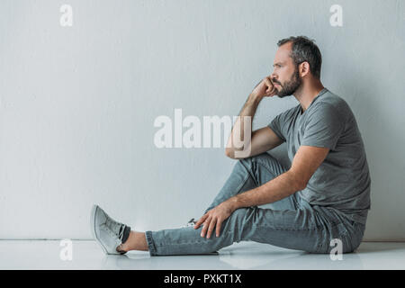 side view of frustrated bearded middle aged man sitting on floor and looking away Stock Photo