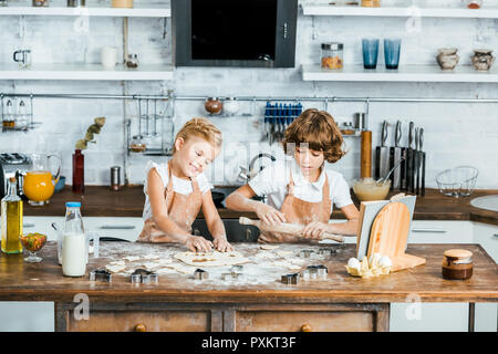 cute happy kids in aprons preparing tasty cookies together Stock Photo