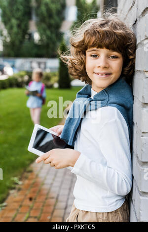 adorable schoolboy using digital tablet and smiling at camera Stock Photo
