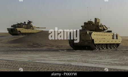 An M1A2 Abrams tank (left) prepares to fire a round while receiving support from a Bradley fighting vehicle during the Company D, 6th Squadron, 9th U.S Cavalry Regiment, 3rd Armored Brigade Combat Team, 1st Cavalry Division, “Hunter Killer” table 12 qualification, June 7, Udairi Range, Kuwait. “Hunter Killer” involves multiple armored vehicles in formation to conduct offensive and defensive firing maneuvers. Stock Photo