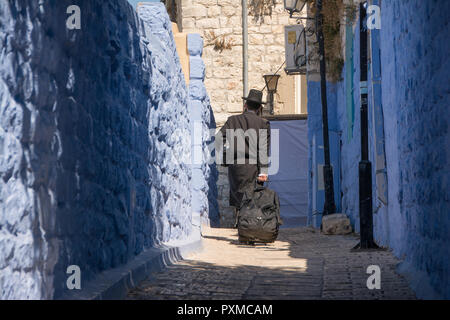 Ultraorthodox jew walking through the blue painted streets of Safed (Tsfat), Israel, with a wheeled suitcase. Stock Photo