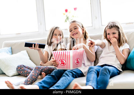 Three happy little girls watching comedy movie on tv and eating popcorn at home Stock Photo