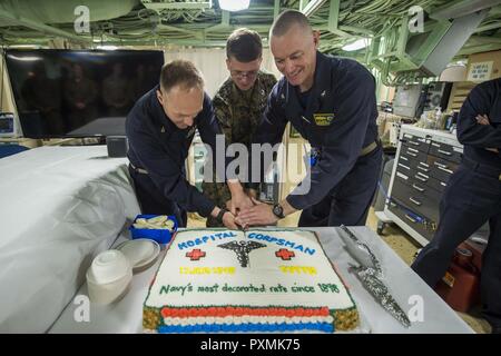 PHILIPPINE SEA (June 17, 2017) Commanding Officer Capt. Nate Moyer (right), Hospitalman Brandon Lyerla (middle), from Carl Junction, Miss., and Senior Chief Hospital Corpsman Charles Marchant (left), from Sylvester, Ga., cut the Hospital Corpsman's 119th birthday cake during a celebration held in medical. Green Bay, part of the Bonhomme Richard Expeditionary Strike Group, is operating in the Indo-Asia-Pacific region to enhance partnerships and be a ready-response force for any type of contingency. Stock Photo