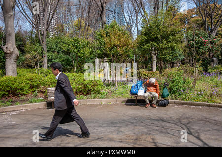 Businessman walking past homeless man sleeping on bench in Shinjuku Chuo Park, Tokyo, Japan Stock Photo