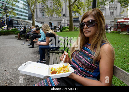 New York City, woman having indian street food on plastic plate in park, lunch break in financial district near wall street Stock Photo
