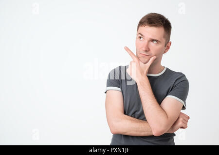 Handsome pensive guy with good-looking hairstyle looking aside and pointing with index finger. Copy space. Stock Photo