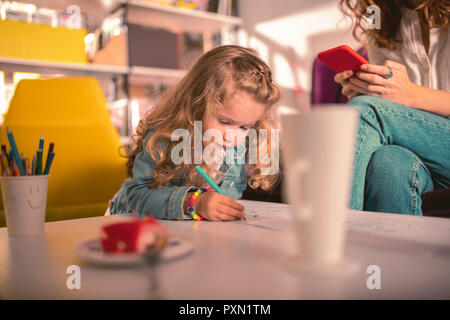 Attentive little girl being busy while drawing her mom Stock Photo