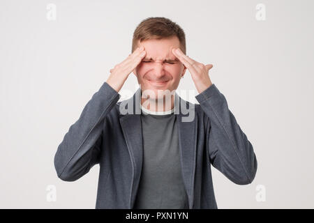 Studio photo of good-looking caucasian man showing how much his head hurts, experiencing pain, looking miserable and exhausted Stock Photo