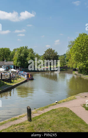 Canal narrowboats moored at the Bottom Basin at Foxton Locks, along with people enjoying the May sunshine outside The Foxton Locks canal side Inn. Stock Photo