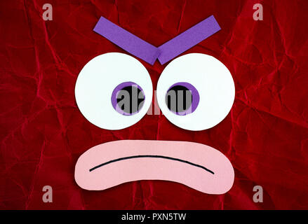 Angry emotional face made from paper. Red background. Stock Photo