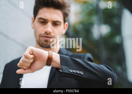 Handsome businessman or student looks at watch. Young man in hurry late for work. Male model on office building background Stock Photo
