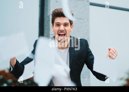 Angry furious male office worker throwing crumpled paper, having nervous breakdown at work, screaming in anger, stress management, mental distress problems, losing temper, reaction on failure Stock Photo