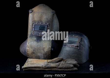 An old mask a protective suit for a welder. Occupational health and safety clothing for production workers on a workshop table. Black background. Stock Photo