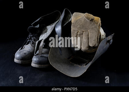 An old mask a protective suit for a welder. Occupational health and safety clothing for production workers on a workshop table. Black background. Stock Photo