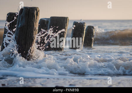 Low angle of abandoned sea defence posts being splashed by waves Stock Photo