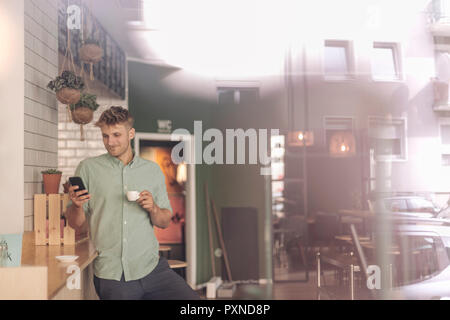 Young business owner drinking coffee, checking smartphone Stock Photo
