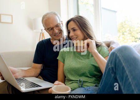 Smiling mature couple sitting on couch at home shopping online with laptop Stock Photo