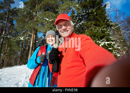 Happy aged active man and woman in sportswear looking at camera in smartphone while making selfie during winter training Stock Photo
