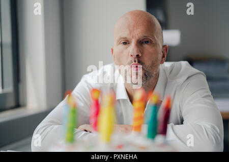 Businessman celebrating his birthday in the office, blowing out candles Stock Photo