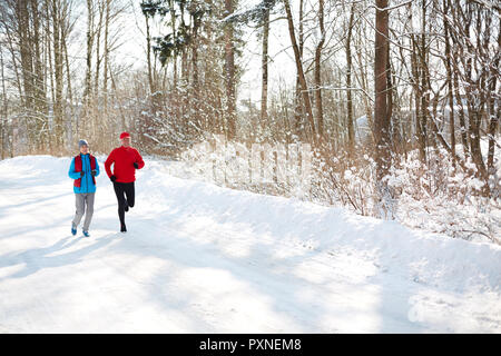 Mature couple in sportswear running down snow road in winter forest in the morning Stock Photo