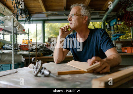 Mature man at workbench in his workshop thinking Stock Photo