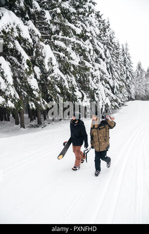 Italy, Modena, Cimone, couple with skiers and snowboard walking in winter forest Stock Photo