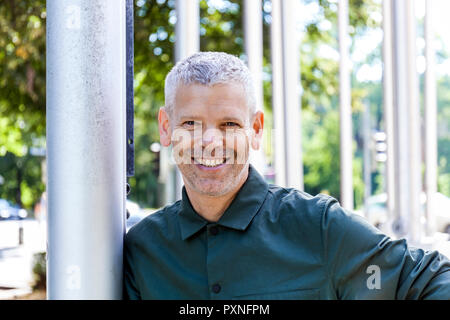 Portrait of a smiling mature man leaning against a pole Stock Photo
