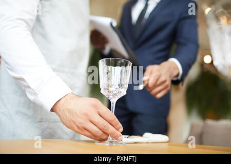 Close-up of waiter puts a wineglass on the table under the supervision of the restaurant manager Stock Photo