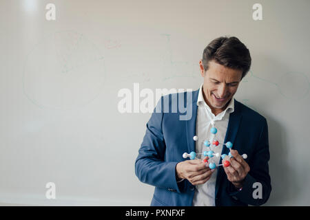 Successful businessman leaning on whiteboard, holding molecule model Stock Photo