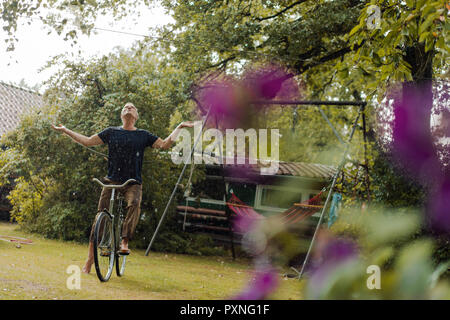 Mature man with bicycle enjoying summer rain in garden Stock Photo