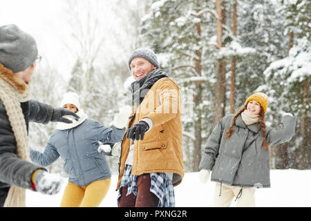 Carefree friends enjoying snowball fight: cheerful excited young man throwing snowball and looking at friend in winter park Stock Photo