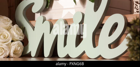 Detail macro of the word "smile" with letters of wood joined and turquoise, in three dimensions and with white flowers as decoration for home Stock Photo