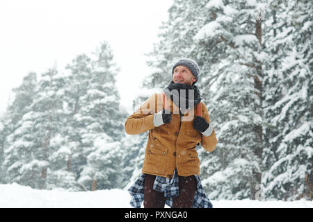 Content excited young male hiker with backpack wearing hat and scarf enjoying winter travel and walking in forest Stock Photo
