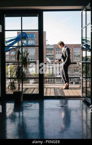 Businessman standing on balcony, using laptop Stock Photo