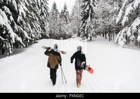 Italy, Modena, Cimone, rear view of couple with skiers and snowboard walking in winter forest Stock Photo