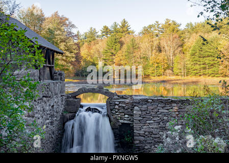 Stone wall and building with waterfall and Autumn trees reflected on Lake in upstate New York. Stock Photo