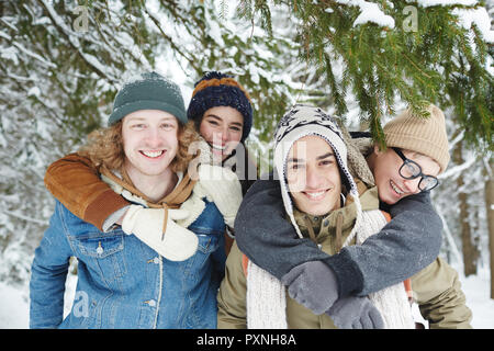 Portrait of two beautiful young couples having fun on winter resort and smiling at camera while posing in snowy forest Stock Photo