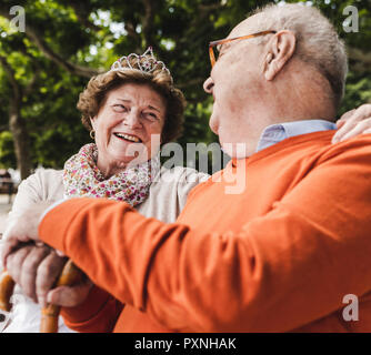 Happy senior couple sitting in park, woman wearing crown Stock Photo