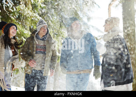Group of happy young people enjoying walk in beautiful winter forest under snowfall  on  vacation Stock Photo