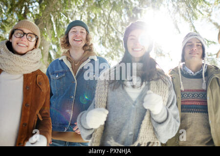Group of four carefree  young people smiling happily enjoying walk in beautiful winter forest on Christmas vacation Stock Photo