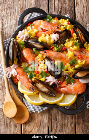 Spanish traditional cuisine: hot paella with seafood shrimps, mussels, fish, and baby octopuses close-up in a frying pan on the table. Vertical top vi Stock Photo