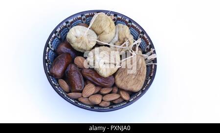 Dried Fruits in an Oriental Bowl. Decorated dish with dried fruit: Figs, dates and natural almonds, Top view, close up, isolated on white background. Stock Photo